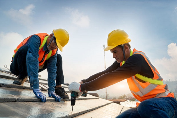 A pair of male construction workers doing work on a roof